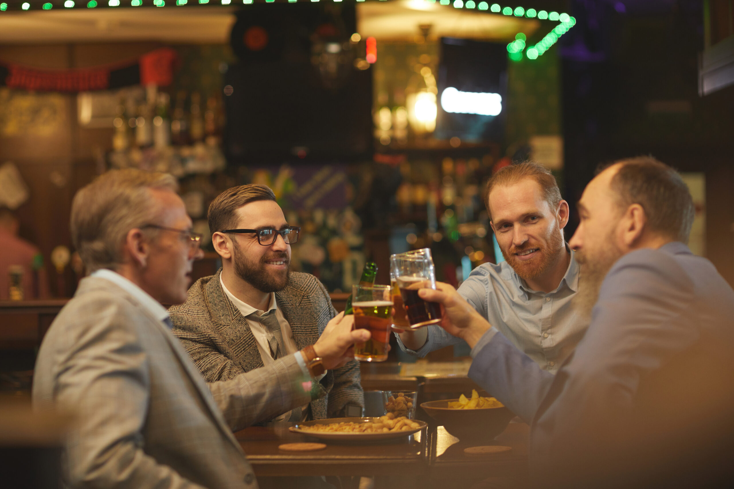 Group of businessmen holding glasses of beer and discussing some working moments in informal setting in the pub